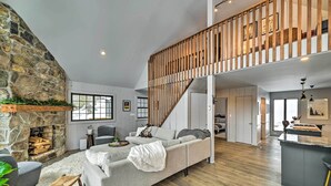 Un vaste espace de vie agrémenté d’une cheminée en pierre, d’un canapé gris et d’un escalier en bois.