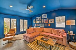 Ein Wohnzimmer mit blauer Wand, einem braunen Ledersessel, einem braunen Leder Sofa, einem Couchtisch mit Schachbrett und einem Deckenventilator.