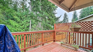 A wooden deck with a lattice railing, surrounded by dense green trees. - Spacious Kent Getaway w/ Yard, Deck + Grill! (Kent)