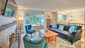 A living room with a fireplace, a sofa with decorative pillows, a wooden coffee table, and a chandelier. - Spacious Kent Getaway w/ Yard, Deck + Grill! (Kent)