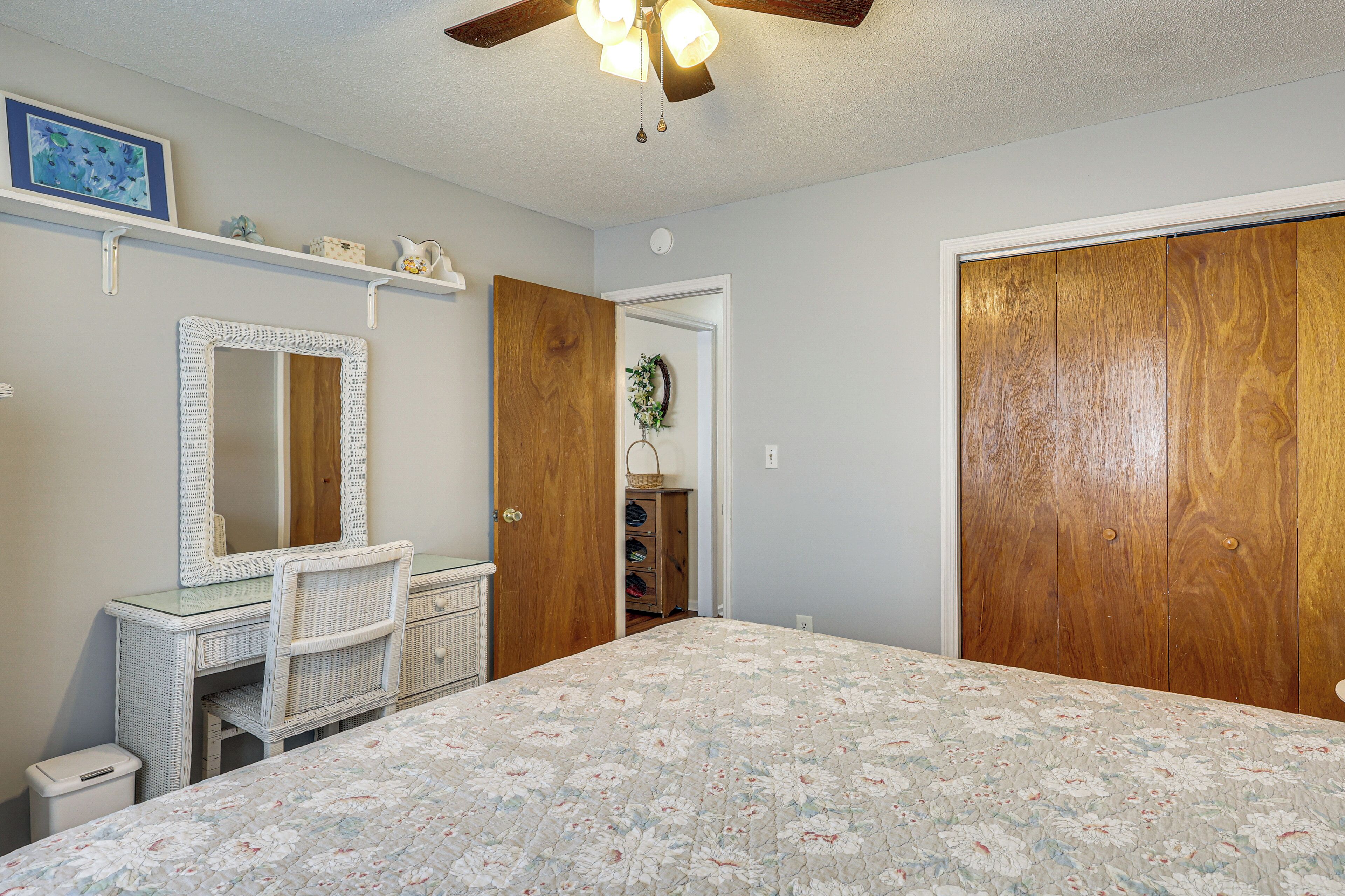 Une chambre à coucher comprenant un lit, une commode, un miroir, une armoire, un ventilateur de plafond et une étagère fixée au mur.