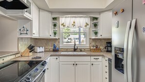 Una cucina con mobili bianchi, forno a incasso, frigorifero in acciaio inossidabile e una finestra con tenda a fiori di girasole.