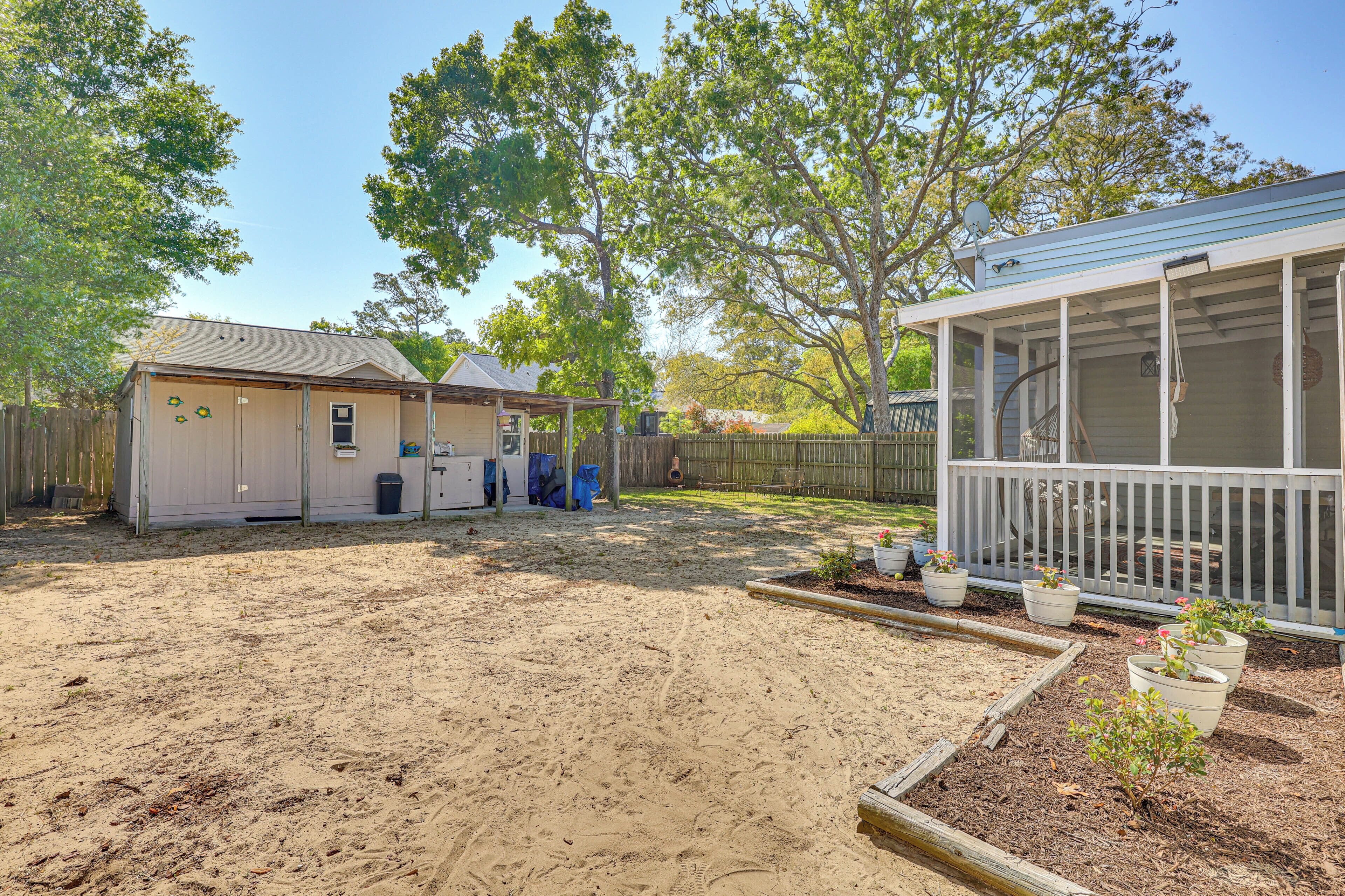 A backyard with a sandy area, a wooden deck, and a small shed.