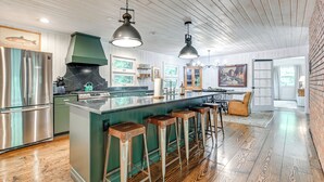 A modern kitchen with a central island, bar stools, stainless steel appliances, and pendant lighting. - Chic Highlands Cabin Retreat w/ Deck + Office! (Highlands)