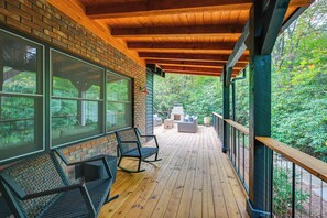 Terraza de madera con mobiliario exterior, ventanas amplias y vistas a la vegetación.