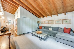Una sala de estar acogedora con un sofá gris, vigas de madera en el techo, una estantería y una mesa de centro con un cuenco.