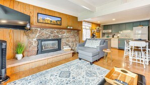 A living room with a stone fireplace, a flat-screen TV, and a grey sofa. - Estes Park Condo w/ Deck & Views ~ 3 Miles to Rmnp (Estes Park)