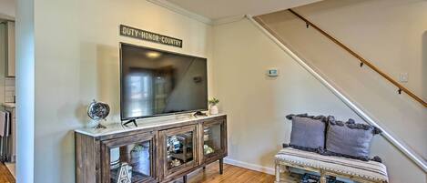 A living room with a flat-screen TV on a wooden console, a bench with cushions, and a staircase.