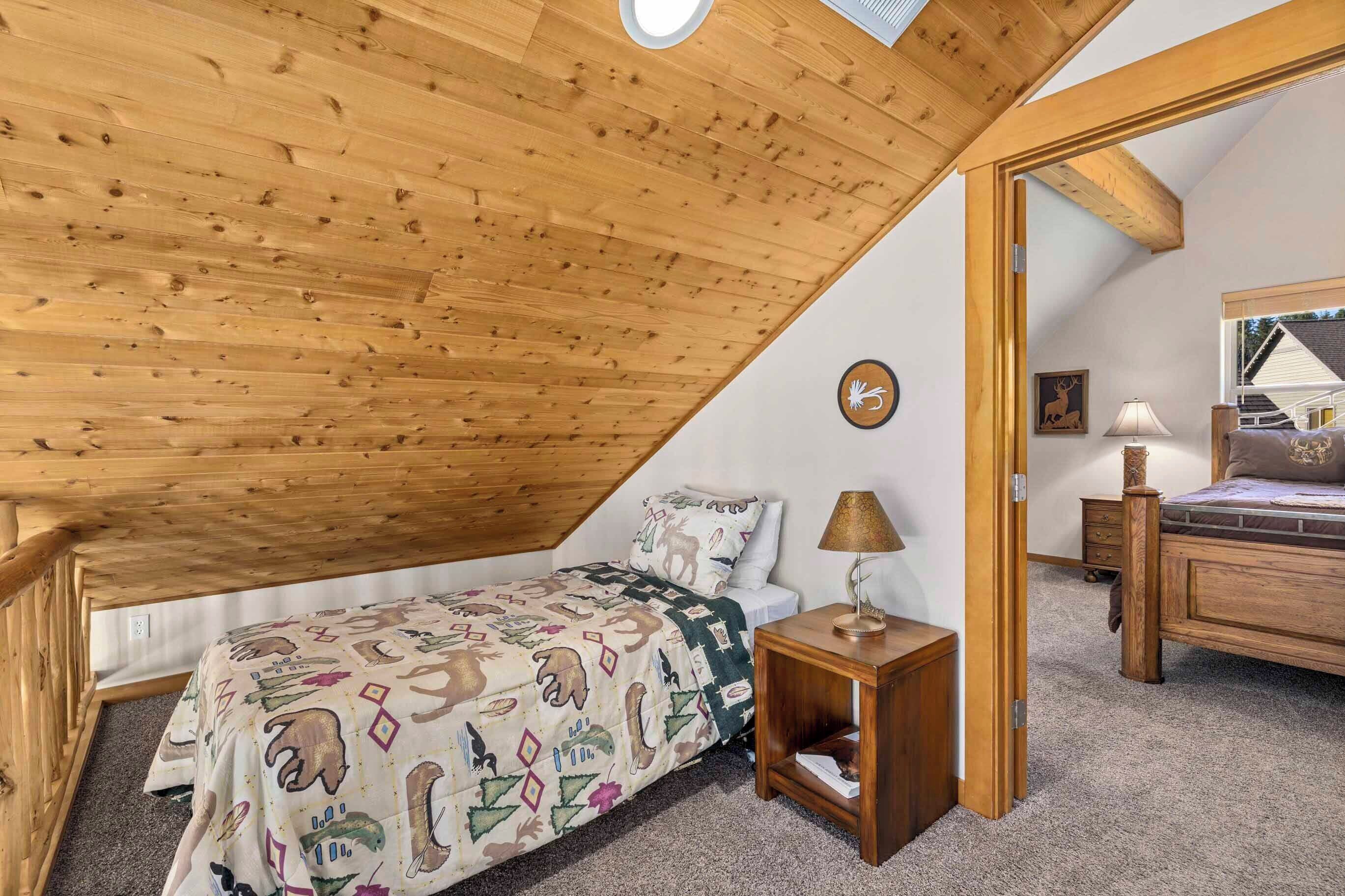A bedroom with a sloped ceiling, a bed with a patterned duvet, a bedside lamp, and a small wooden nightstand.