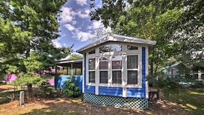 A small, single-story building with a sloped roof and multiple windows, surrounded by trees and a grassy yard.