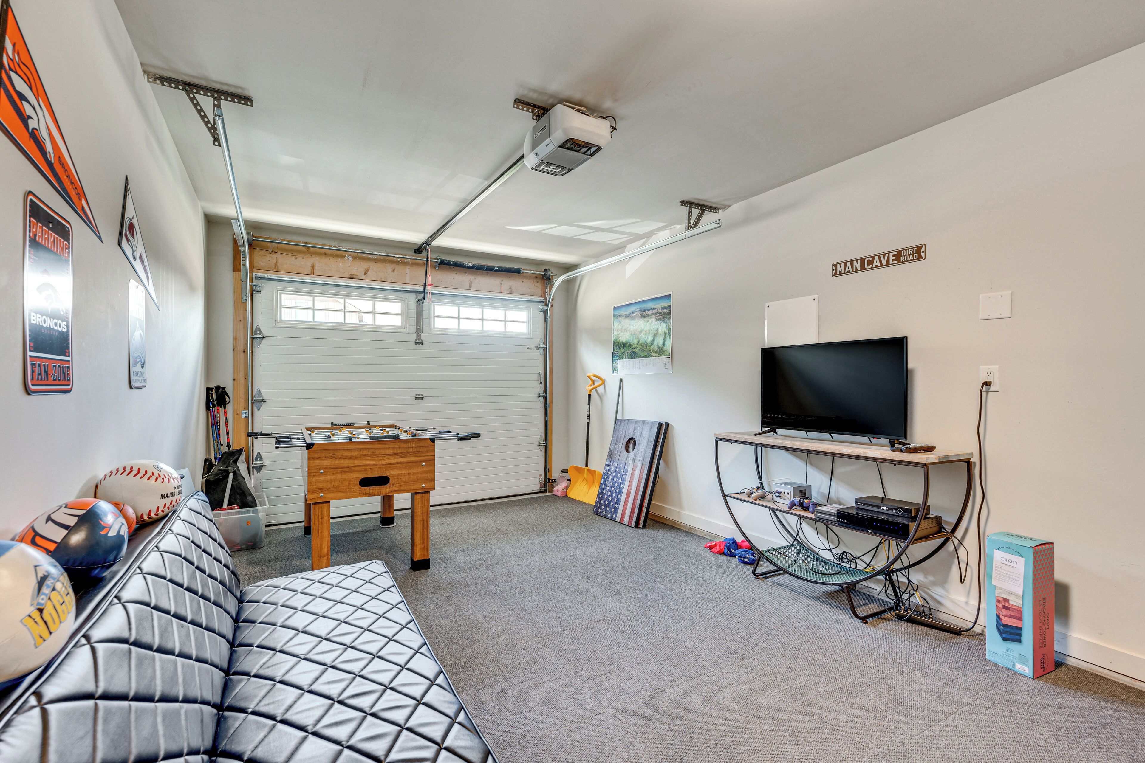 A living room with a sofa, a foosball table, a television, and a wall-mounted shelf.