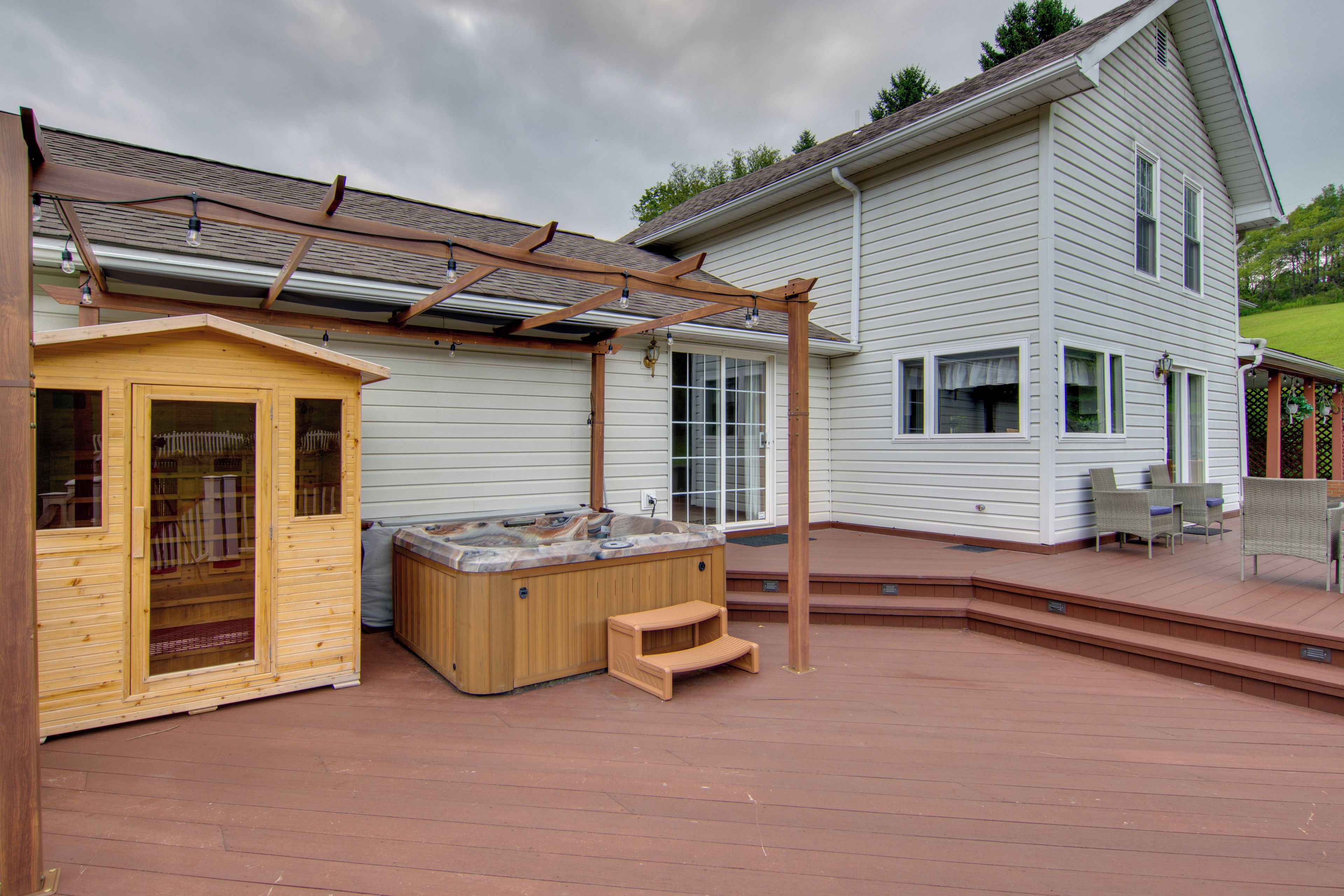 Un bain à remous en bois et une cabane de jeux en bois se trouvent dans un jardin, agrémentés d’une pergola, d’un autre bain à remous et d’un espace patio.