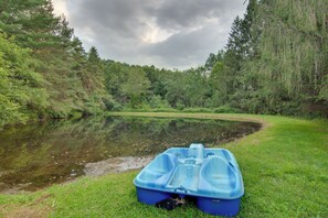 Un petit bateau gonflable bleu est amarré sur une berge herbeuse, au bord d’une rivière paisible, entourée d’une forêt dense.