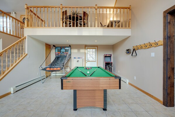 A pool table in a spacious room with a staircase leading to an upper level.