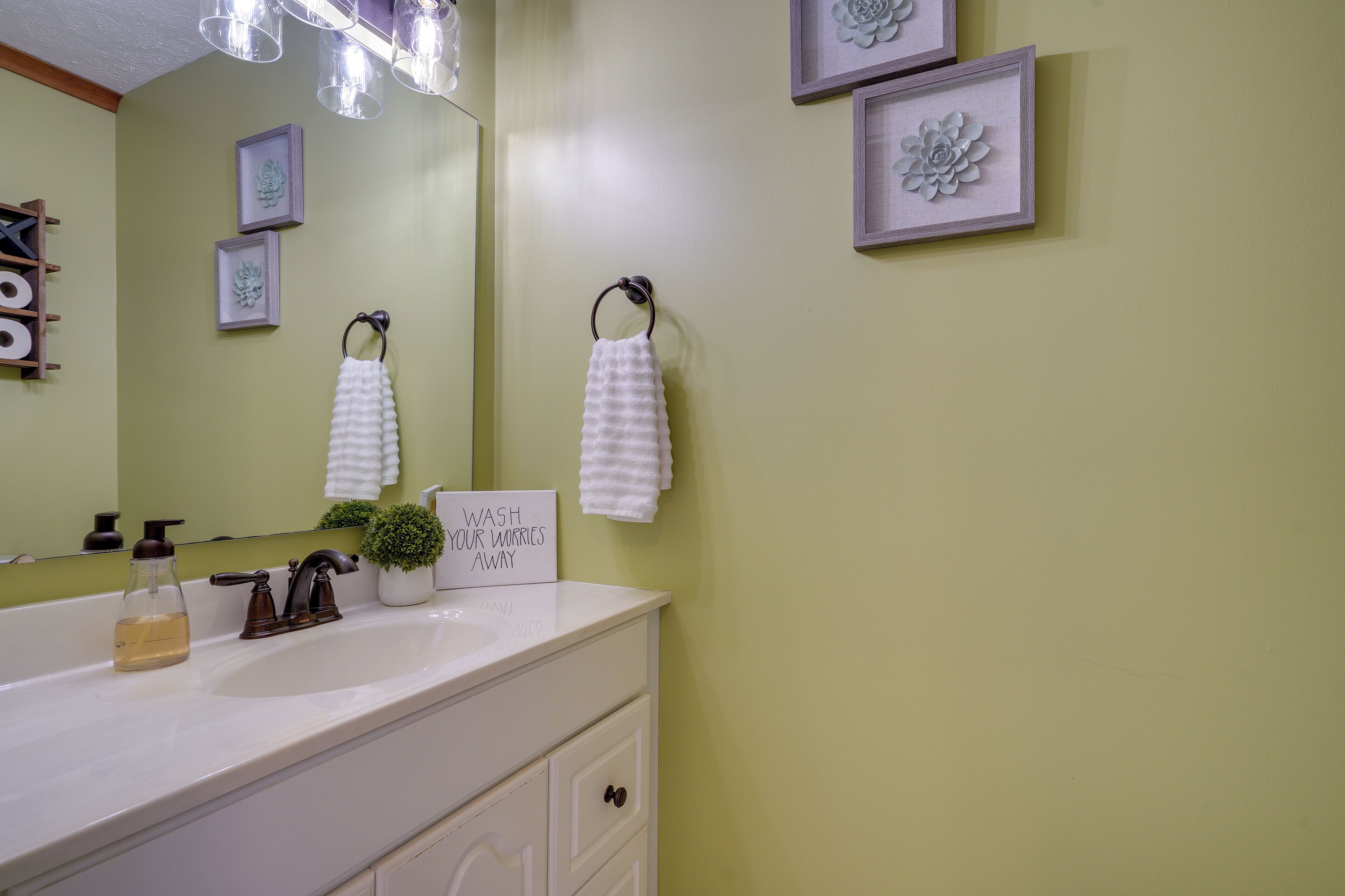 Un baño con un lavamanos blanco, un espejo, un perchero para toallas y un letrero que dice 'WASH YOUR WORRIES AWAY'.