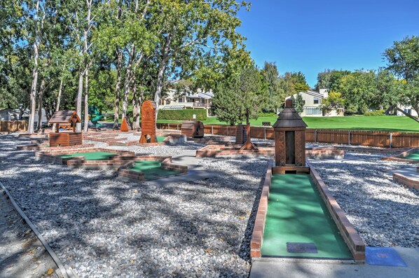 A playground with wooden play structures, a green rubber surface, and a gravel area.