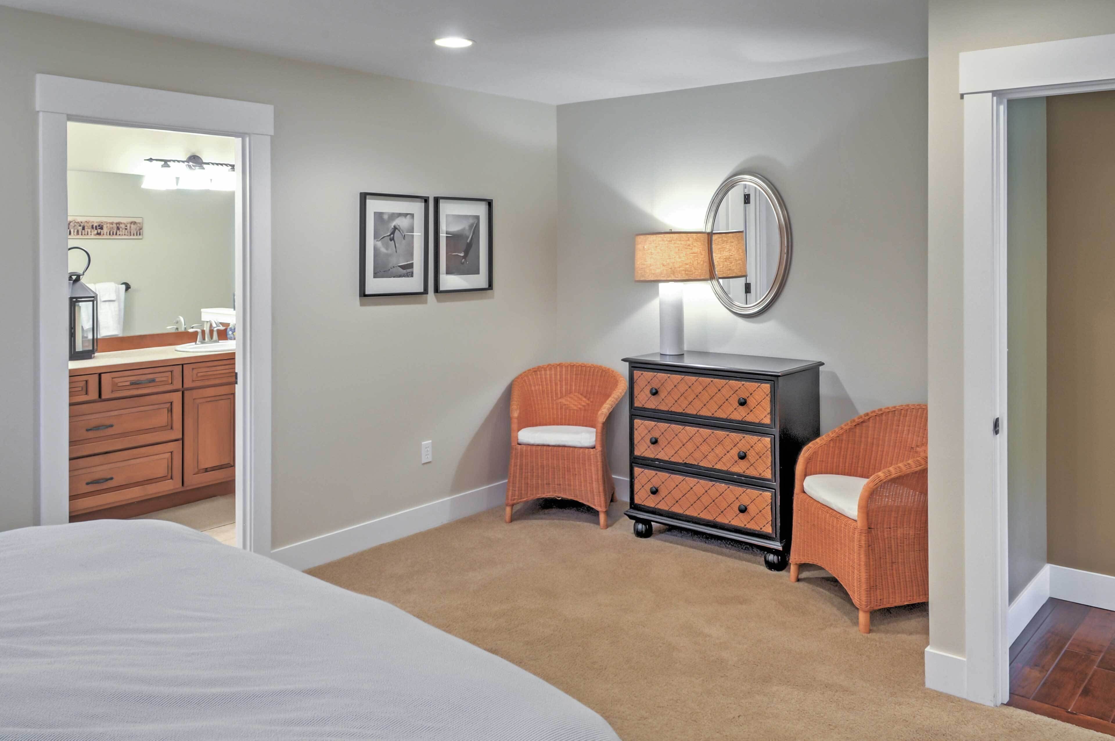 A bedroom with a bed, a dresser, two wicker chairs, a mirror, and framed pictures on the wall.