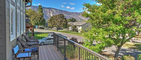 A wooden deck with wicker furniture, a view of a mountain, and a residential street.