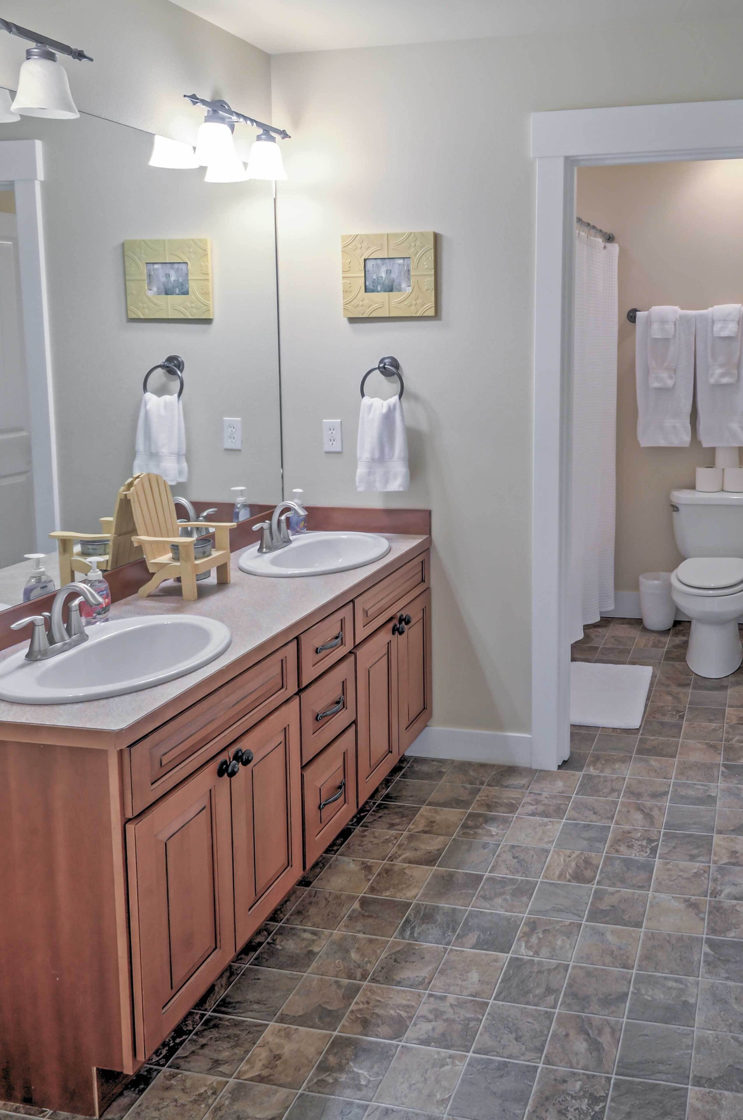 A bathroom with two sinks, a wooden vanity, a mirror, and a shower area.