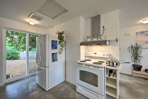 A compact kitchen with a refrigerator, stove, and oven, a small shelf with kitchen utensils, and a potted plant. - Sleek Cottage By Seattle's Top Sights, Lumen Field (Seattle)