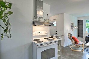 A modern kitchen with a white stove, a built-in oven, and a stainless steel range hood. There is a plant on the left and a chair with a red cushion in the background. - Sleek Cottage By Seattle's Top Sights, Lumen Field (Seattle)