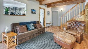 A living room with a wooden floor, a brown leather sofa, a leather armchair, a small wooden side table, and a wall-mounted shelf with plants and a sign. - Cozy Ashford Home - 5 Mi to Rainier Nat'l Park! (Mineral)