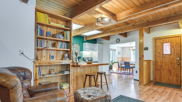 A cozy living room with a leather armchair, a brown ottoman, a wooden bookshelf, and a kitchen area with a bar. - Cozy Ashford Home - 5 Mi to Rainier Nat'l Park! (Mineral)