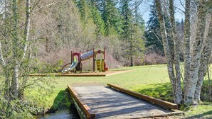 A wooden bridge over a stream leading to a playground with slides and swings. - Cozy Ashford Home - 5 Mi to Rainier Nat'l Park! (Mineral)