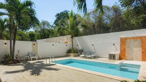 Una piscina con bordeado de baldosas, rodeada por un muro blanco con sección de ladrillo y palmeras.