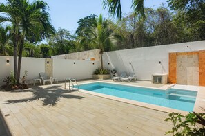 Una piscina con bordeado de baldosas, rodeada por un muro blanco con sección de ladrillo y palmeras.