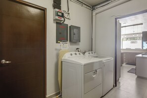 A laundry room with two front-loading washing machines, a dryer, and a wall-mounted electrical panel.