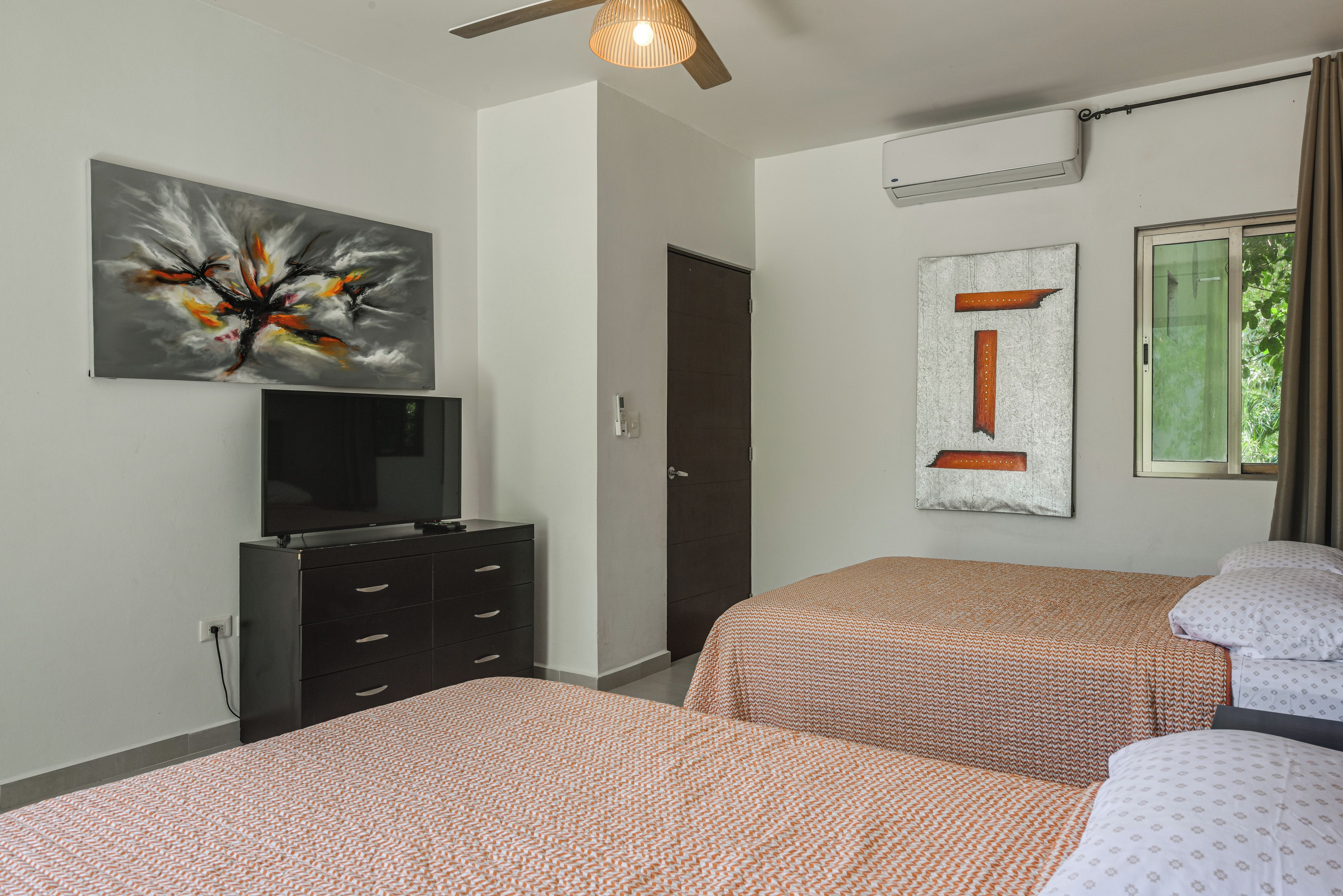 Een slaapkamer met twee bedden, een televisie op een dressoir en kunstwerken aan de wanden.