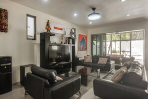 A modern living room with a flat-screen TV, black leather sofas, and a large window providing a view of the outdoors.