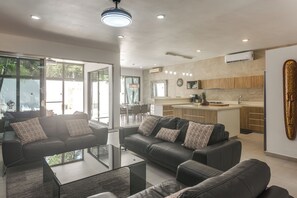 A modern living room with a glass coffee table, black sofas, and a dining area with chairs. - 1 Mi to Beach: Luxe Playa Del Carmen Home w/ Pool (Playa del Carmen)
