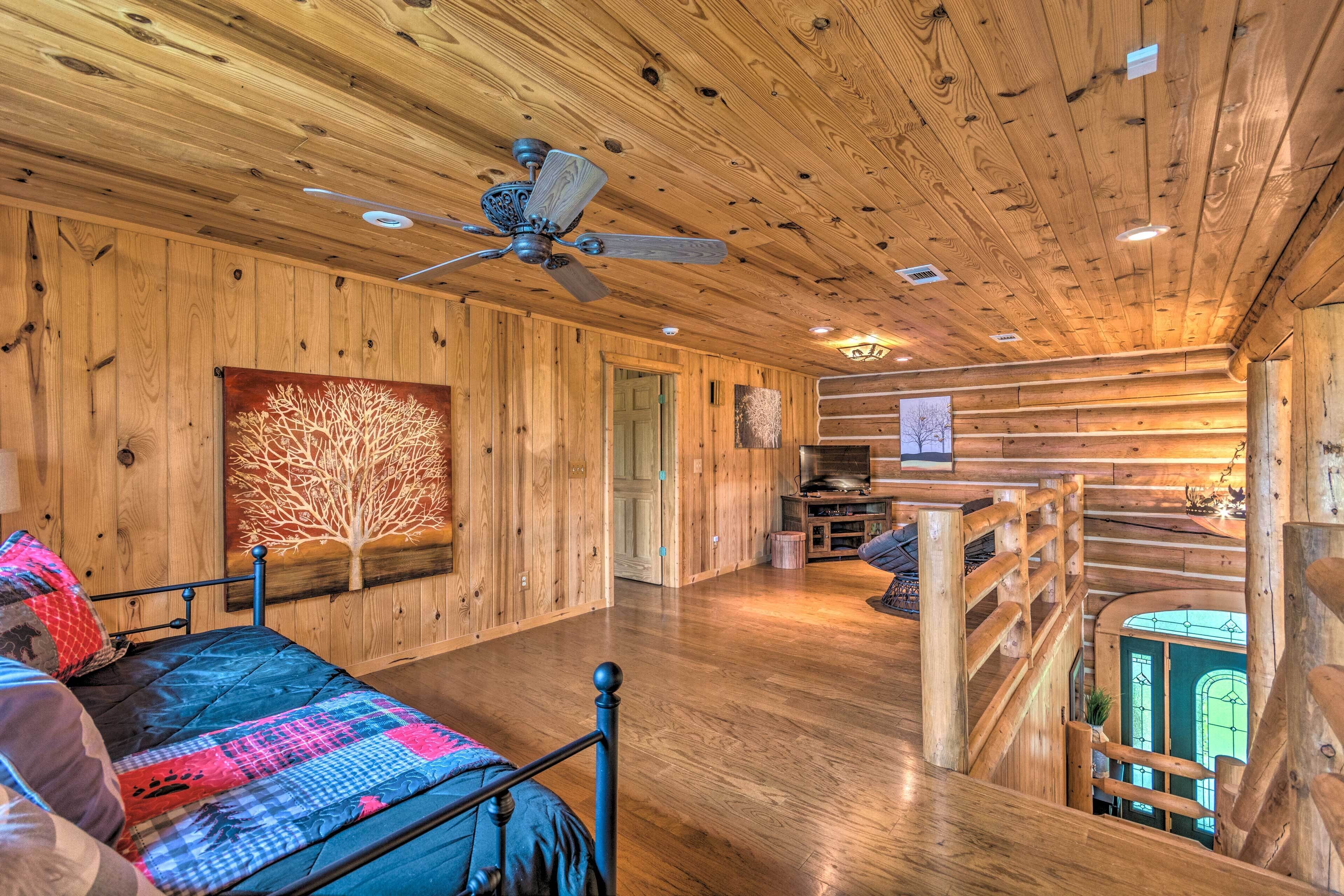 A spacious room with a wooden ceiling, a bed with a colorful quilt, a ceiling fan, and a staircase leading to an upper level.