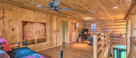 A spacious room with a wooden ceiling, a bed with a colorful quilt, a ceiling fan, and a staircase leading to an upper level.