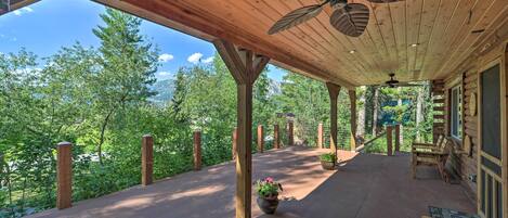 A covered porch with a ceiling fan, wooden beams, and a view of a forested mountain area.