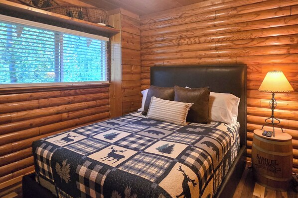 A log cabin-style room with a bed, a window with blinds, a lamp on a wooden barrel, and a quilt with animal prints. - Alpine Winter Wonderland! Log Cabin w/ Views (Alpine)