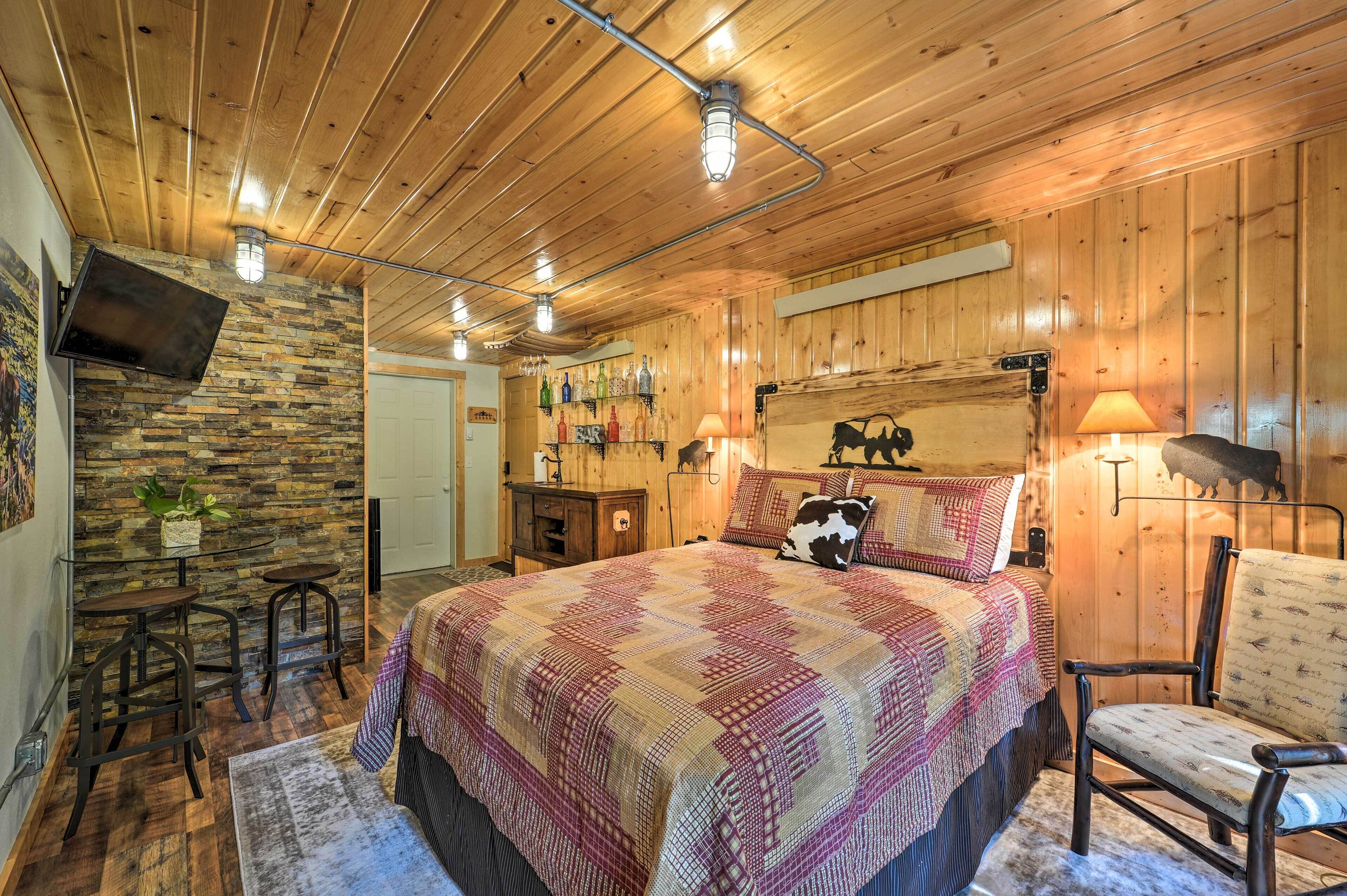 A cozy wooden room with a bed, a chair, a stone wall, and a bar area with bottles.