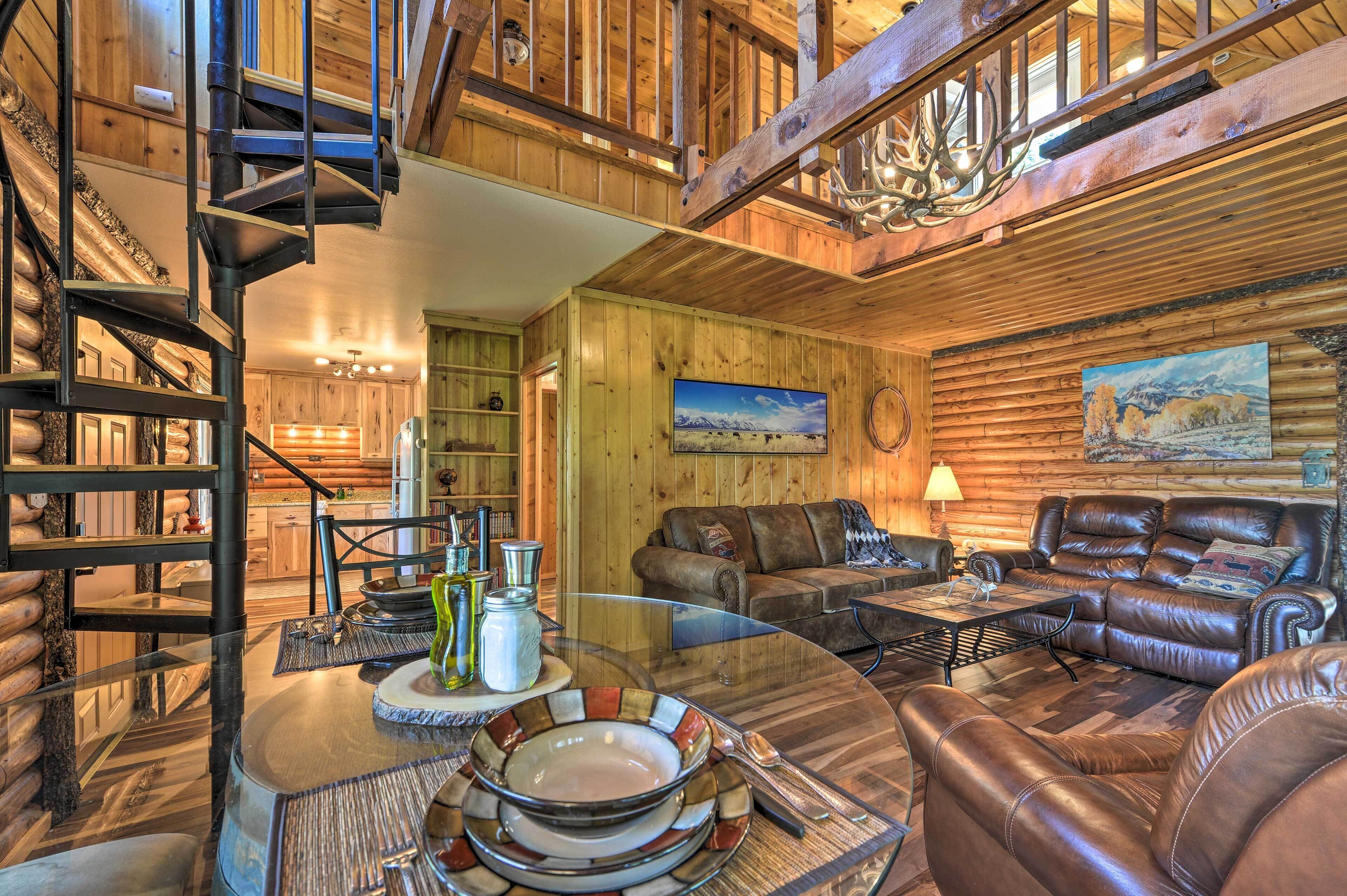 A log cabin interior with a wooden staircase, leather sofa, dining table, and a painting on the wall.