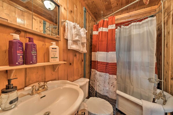 A wooden bathroom with a bathtub, toilet, and sink. There are bottles of shampoo and soap on the sink. - Alpine Adventures: Cozy Log Cabin w/ Deck & Views! (Alpine)