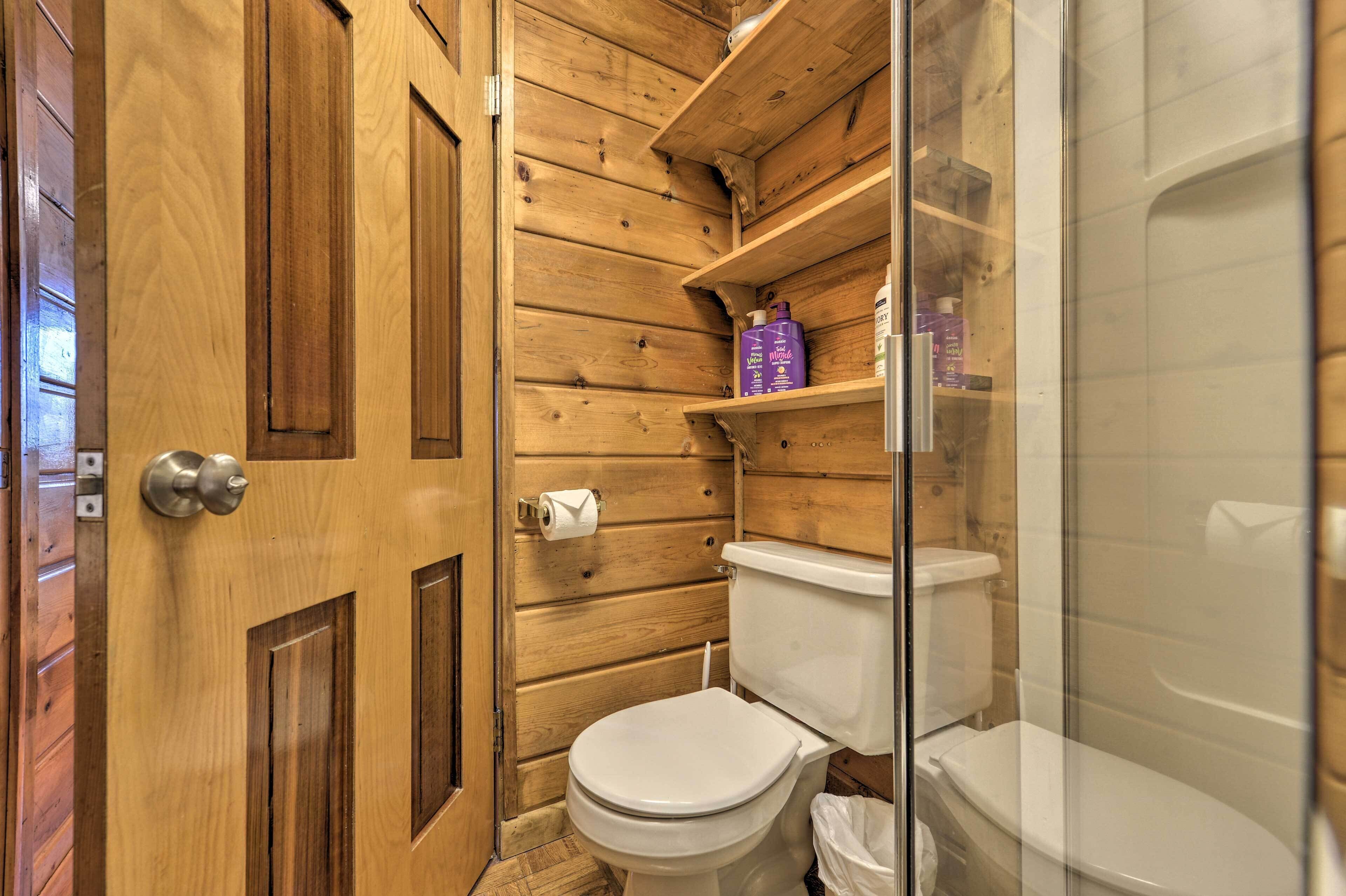 Un baño revestido de paneles de madera con un inodoro, una cabina de ducha y estantes con artículos de aseo.