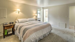 A bedroom with a bed, bedside lamps, a nightstand with books, and a door leading to another room. - Spacious Family Home on Golf Course: Hike & Bike! (Bremerton)