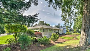 A house with a covered porch, surrounded by a well-maintained lawn and various shrubs. - Spacious Family Home on Golf Course: Hike & Bike! (Bremerton)