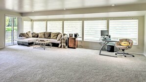 A spacious living room with a large window, a sofa, a coffee table, and a desk with a chair. - Spacious Family Home on Golf Course: Hike & Bike! (Bremerton)