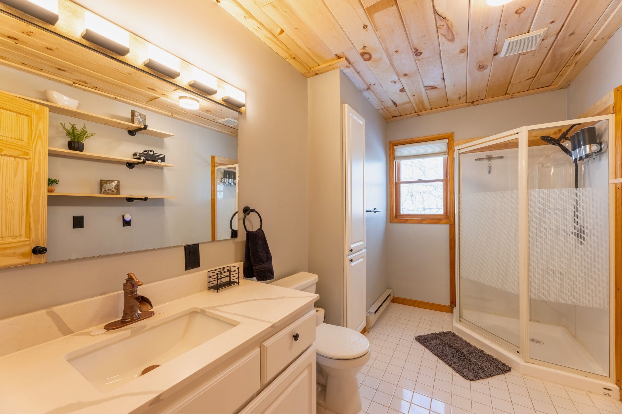 A modern bathroom with a wooden ceiling, white fixtures, a glass shower enclosure, and a small window.