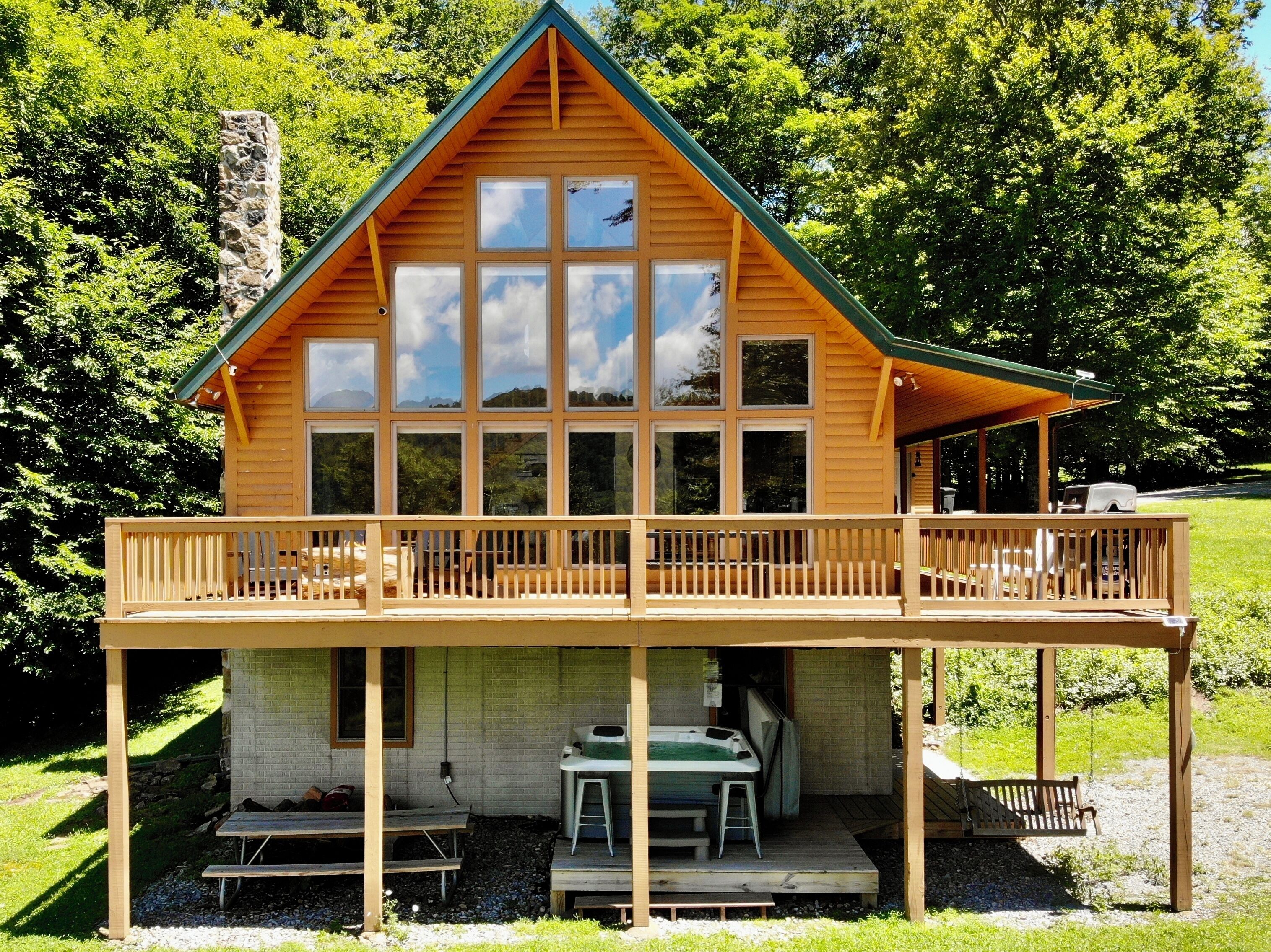 A wooden cabin with a balcony, a hot tub, and a covered outdoor seating area.