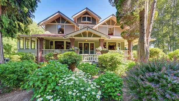 A two-story house with a porch, surrounded by a garden with various plants and flowers. - Historic Auburn House on 37 Acres w/ Private Lake! (Kent)
