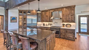 A spacious kitchen with wooden cabinets, a large island with seating, and a stainless steel refrigerator. - Spacious Big Sky Cabin w/ Hot Tub & Grill! (Big Sky)