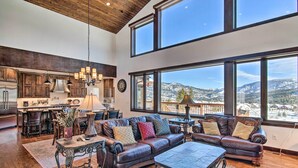A spacious living room with a large window overlooking a snowy mountain. - Spacious Big Sky Cabin w/ Hot Tub & Grill! (Big Sky)
